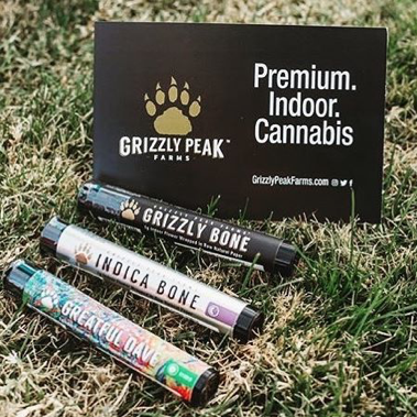 Three pre-rolls in joint tubes lying on the grass in front of a cusotm package