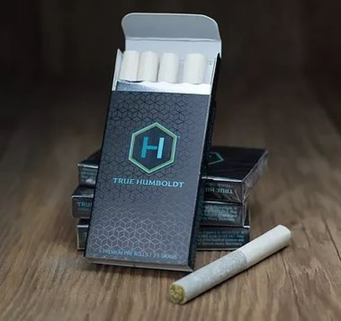 Multiple pre-roll packages stack on top of each other with an open one in the front conatining four pre-rolled tubes. One is on the table as well